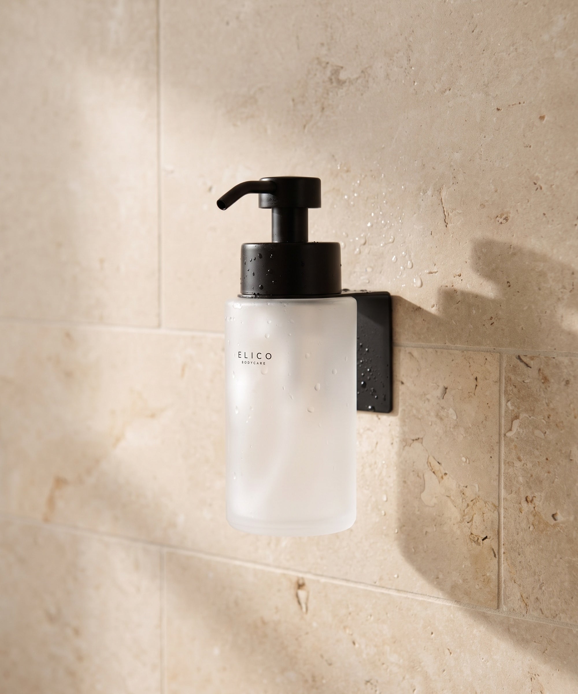 Frosted Elico Bodycare dispenser in the matte black wall mount on a limestone shower wall