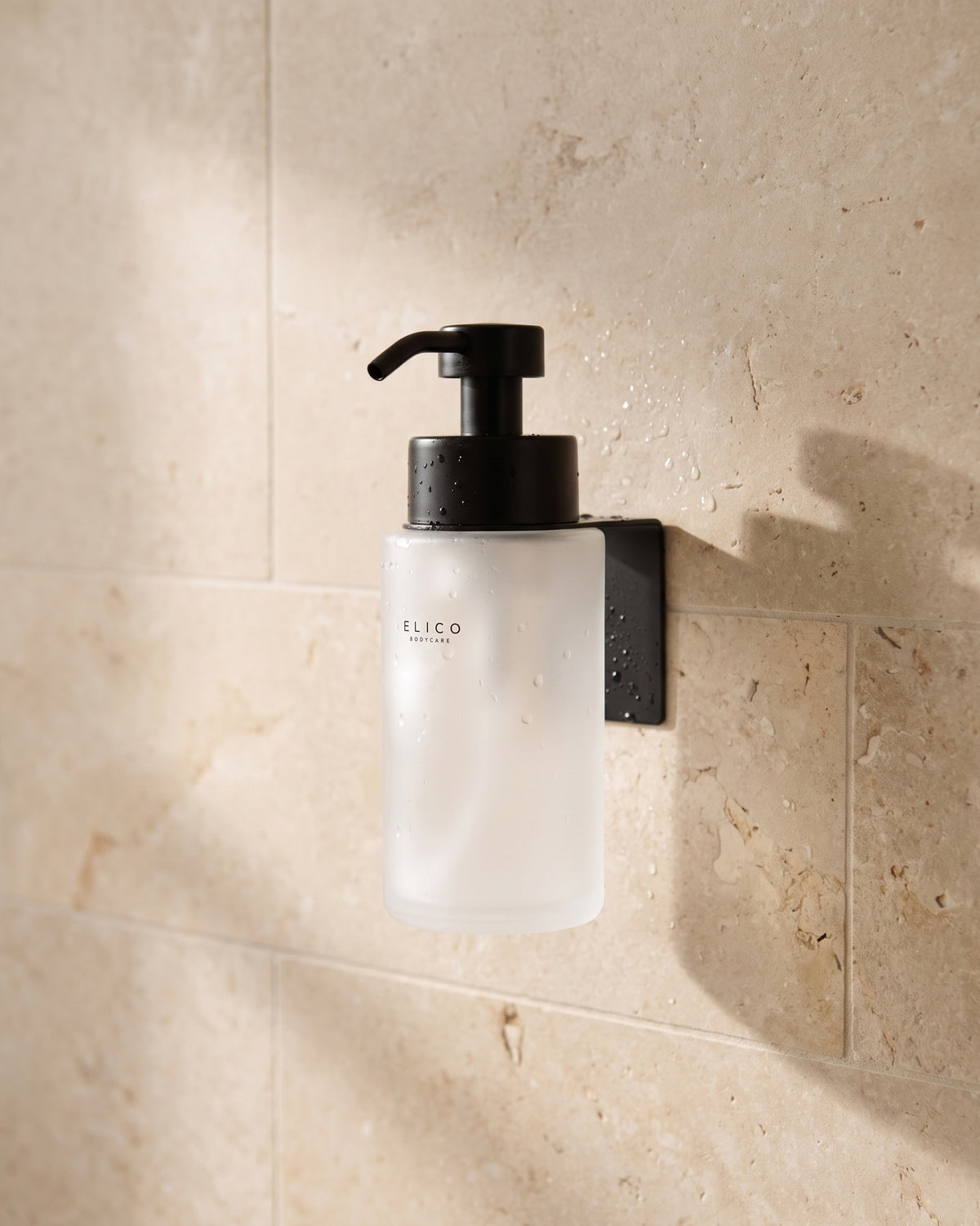 Frosted Elico Bodycare dispenser in the matte black wall mount on a limestone shower wall
